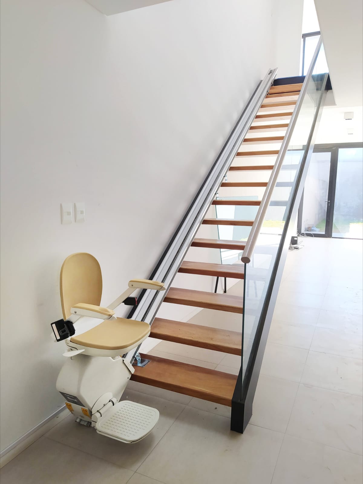 Silla salvaescaleras recta instalada en escalera de madera con baranda de vidrio